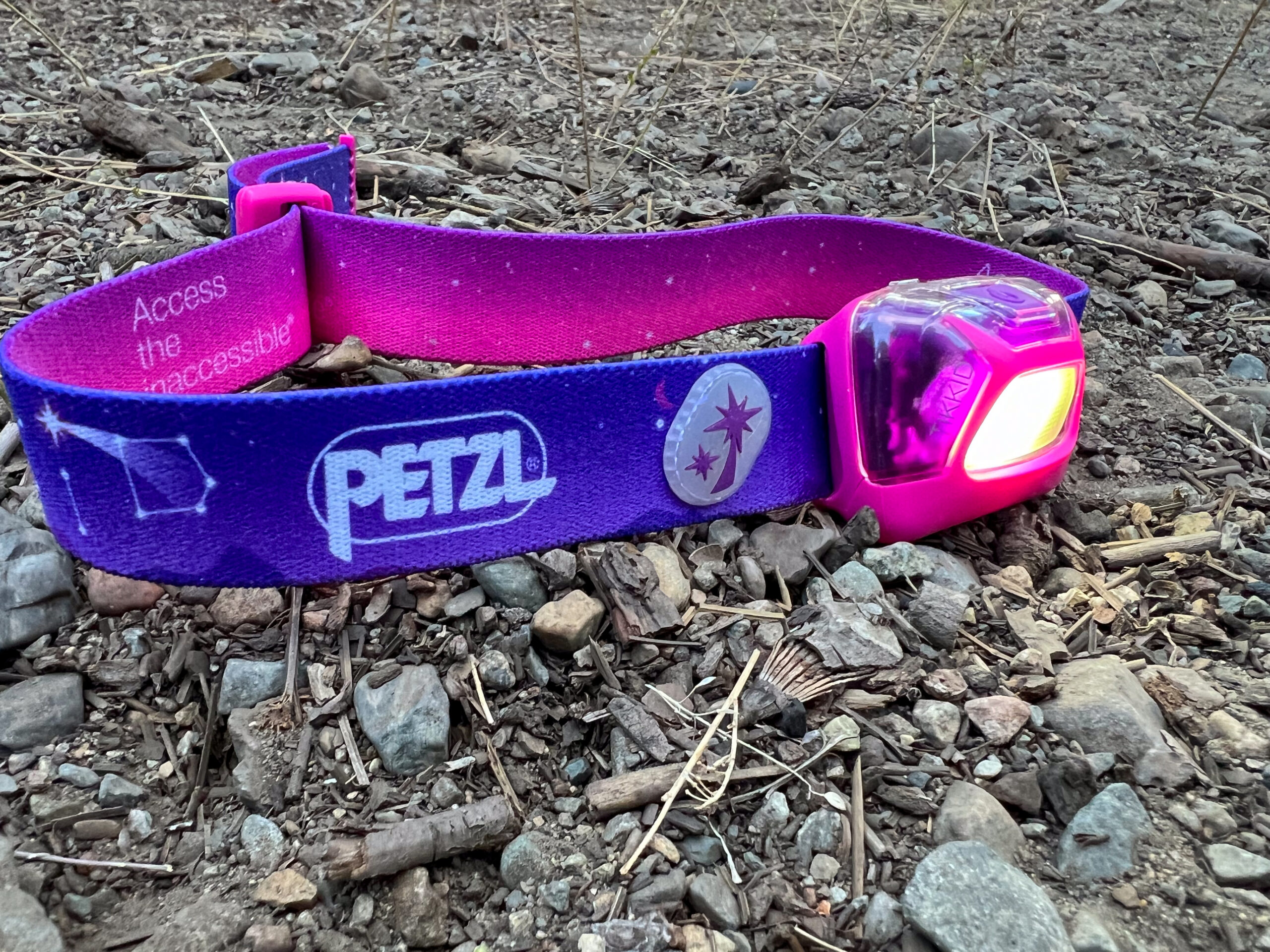 The image shows the Petzl Tikkid headlamp sitting on the forest floor. The light is turned on.