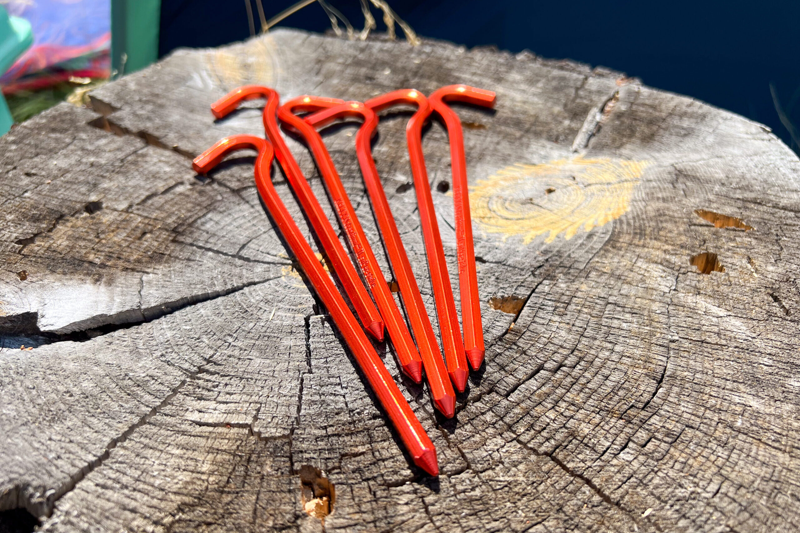 The image shows 6 red tent stakes on a tree stump.