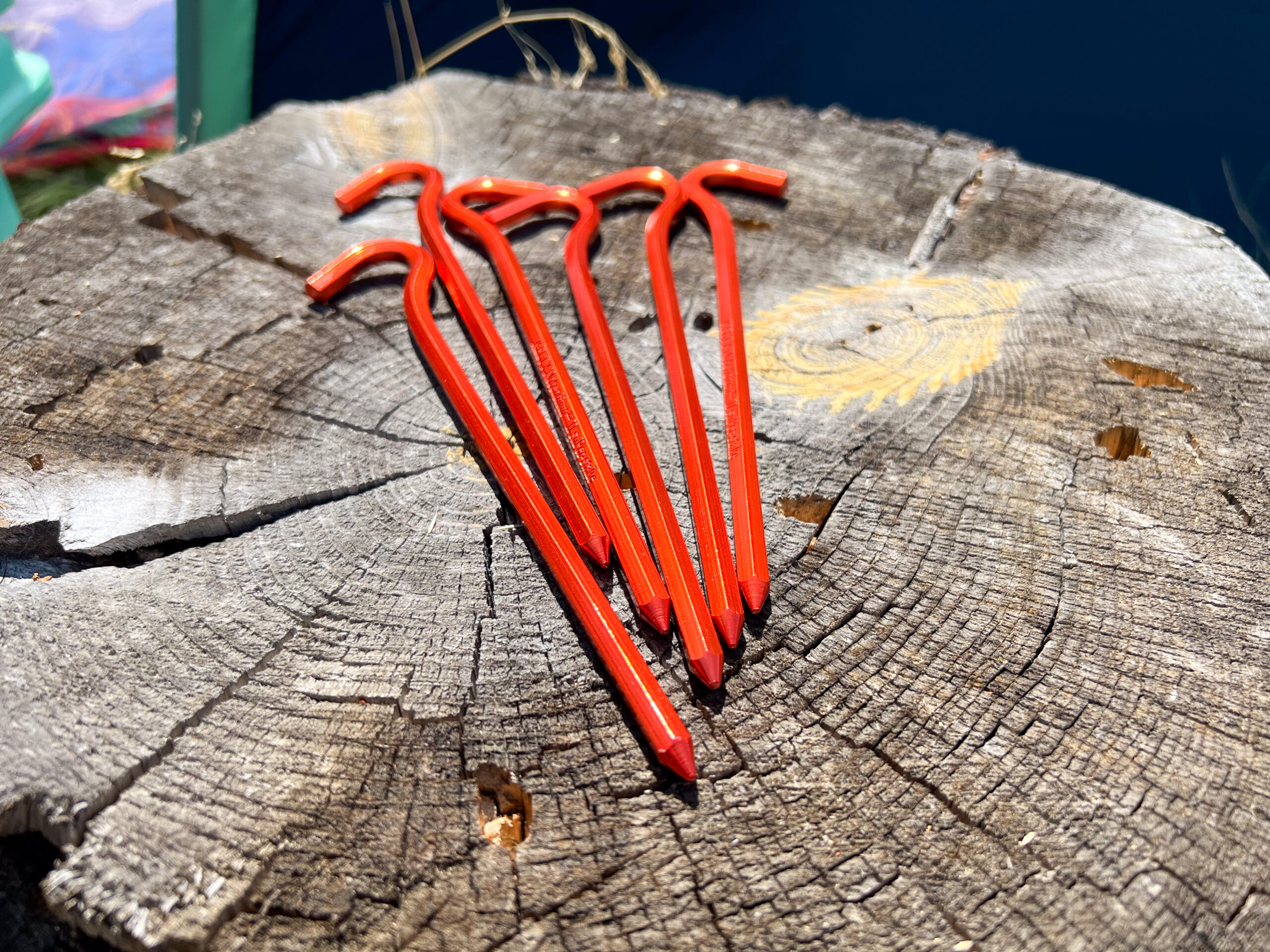 The image shows 6 red tent stakes on a tree stump.