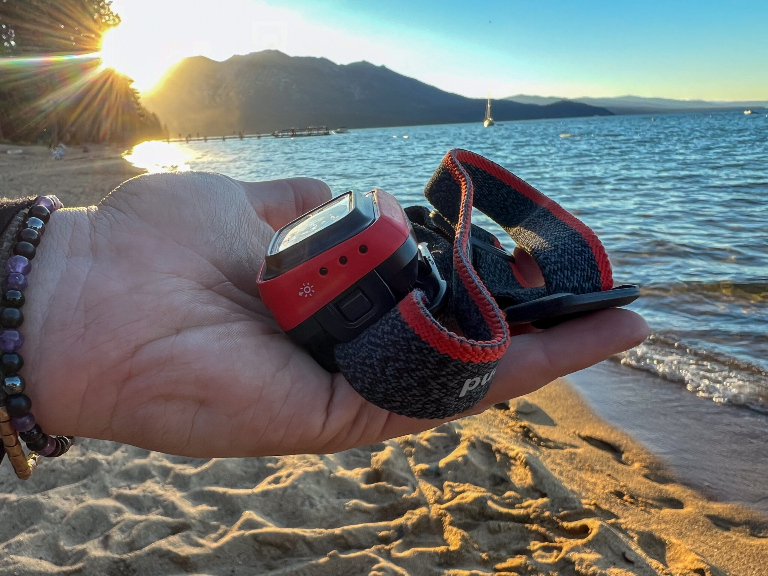 The image shows a Spot 400 in the hand of a camper. The camper is on a beach, the sun is setting, and the side battery life indicator is featured in the photo.