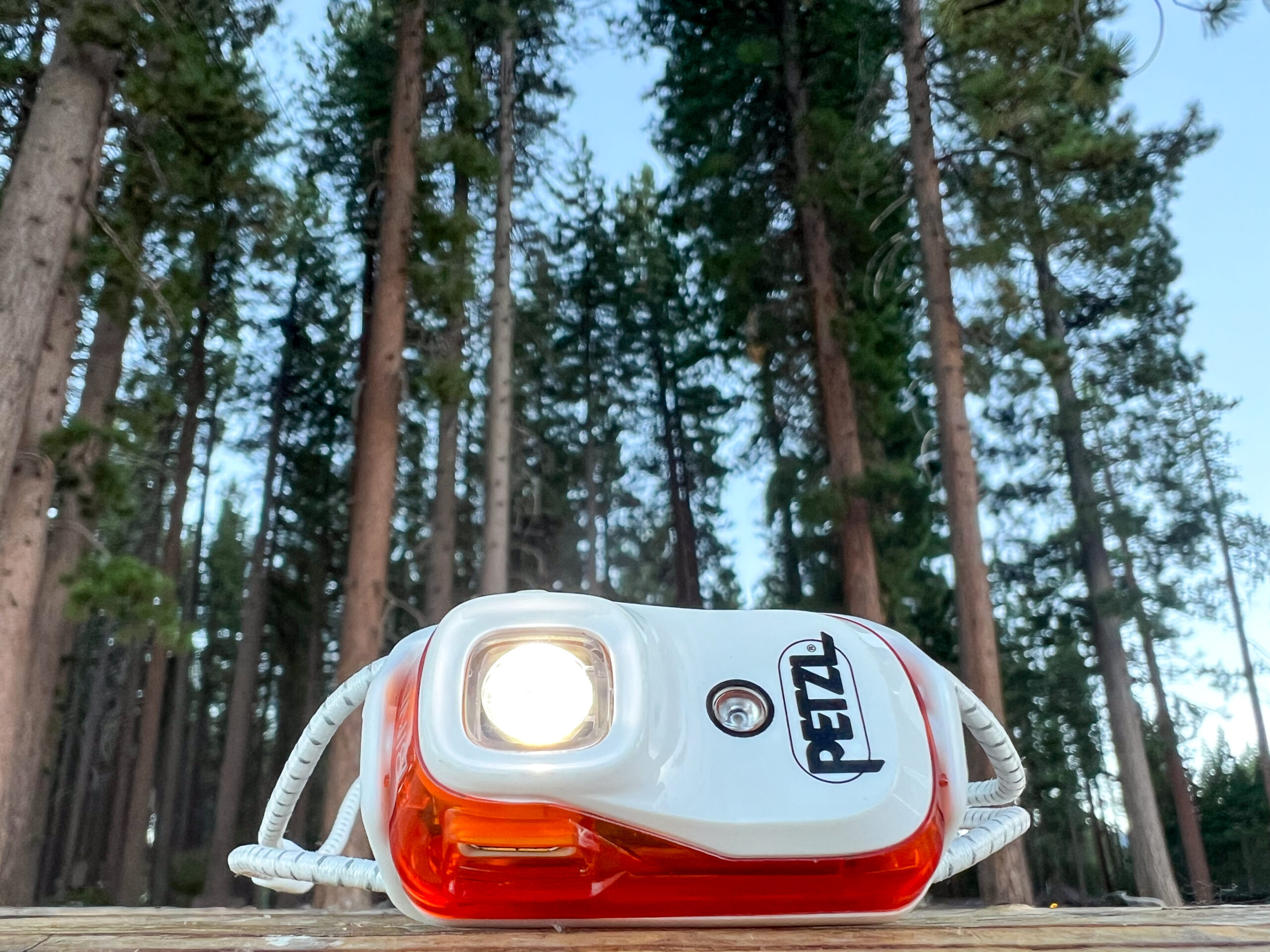 The image shows a Petzl Bindi headlamp with it's light on. The headlamp is sitting on a table and its pointed towards the sky.