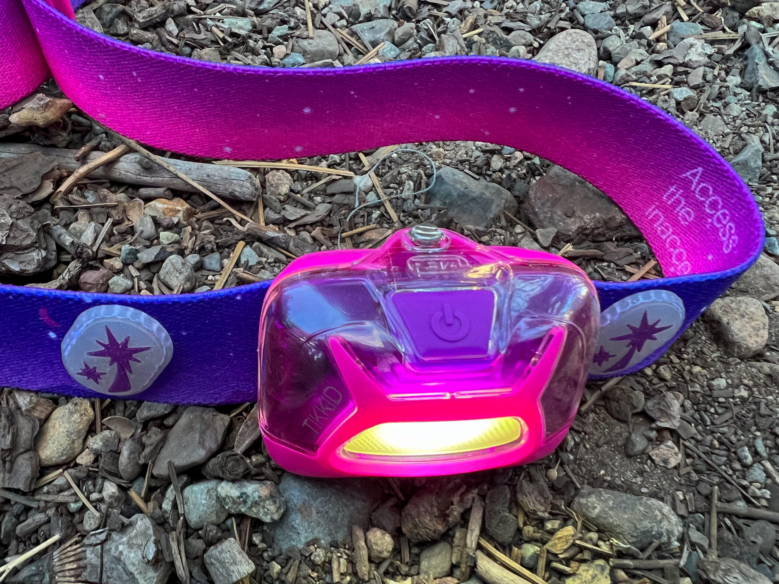 The image shows the Petzl Tikkid headlamp sitting on the forest floor. The light is turned on.