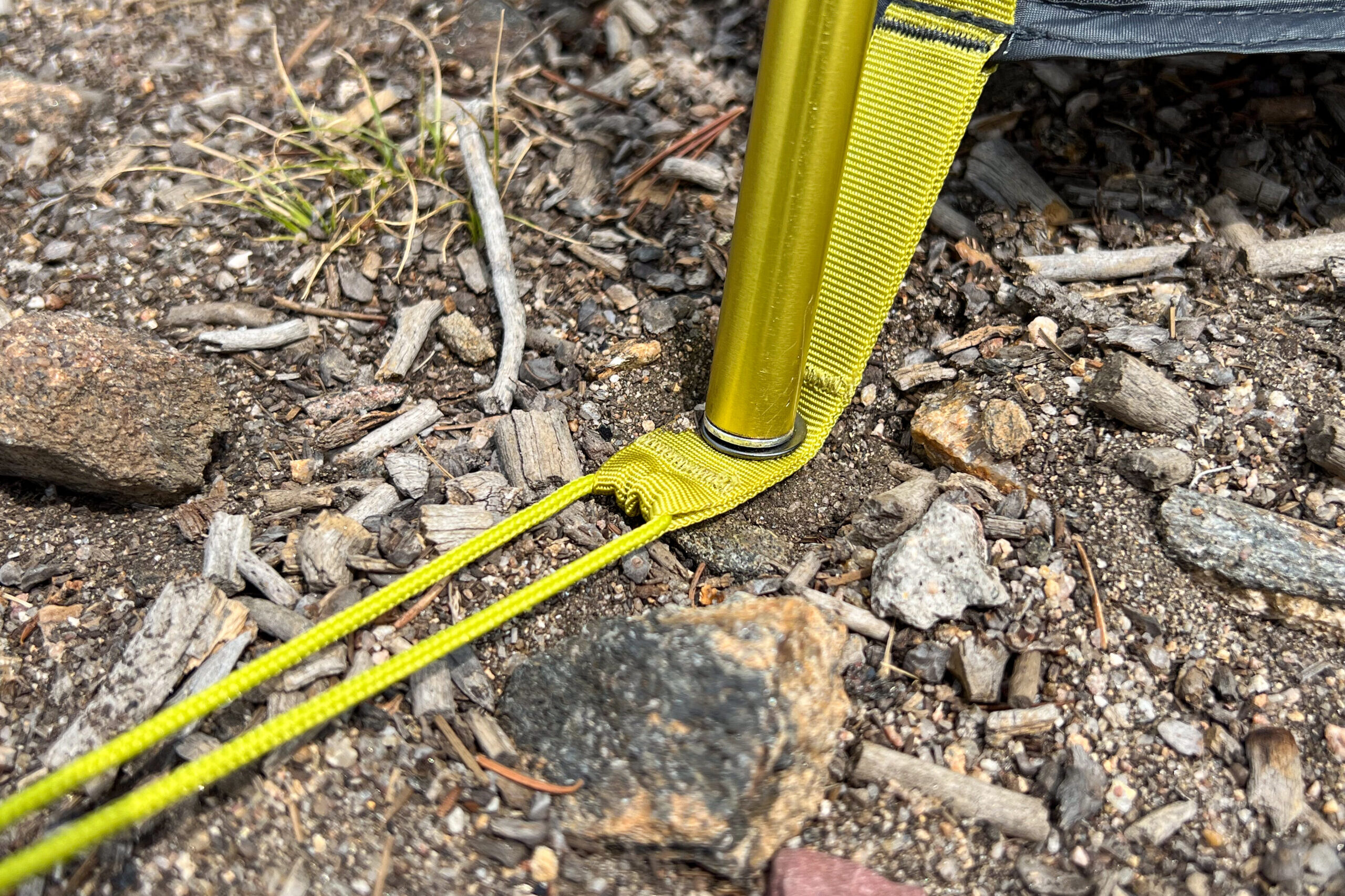 A imagem mostra um mastro de barraca que foi colocado em um ilhós dentro de uma cinta amarela.