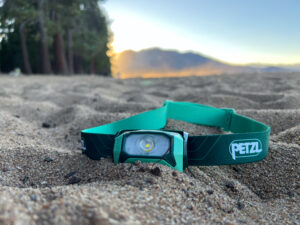 The image shows the Petzl Tikkina headlamp sitting the sand.