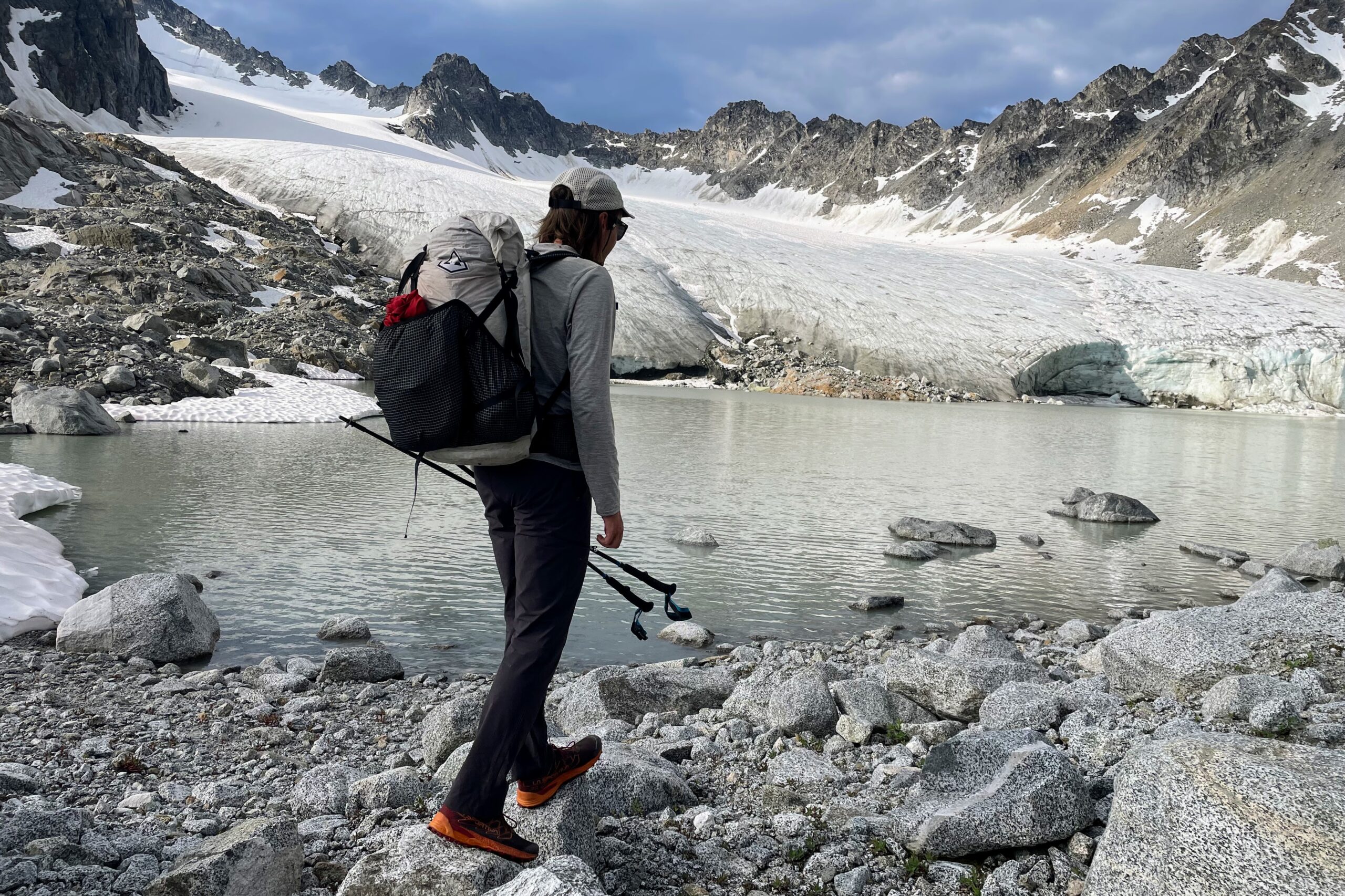 A man stands in front of a glacier facing away from the camera.