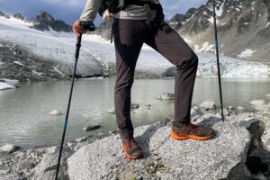 A man shows the front of pants in front of a glacier lake.