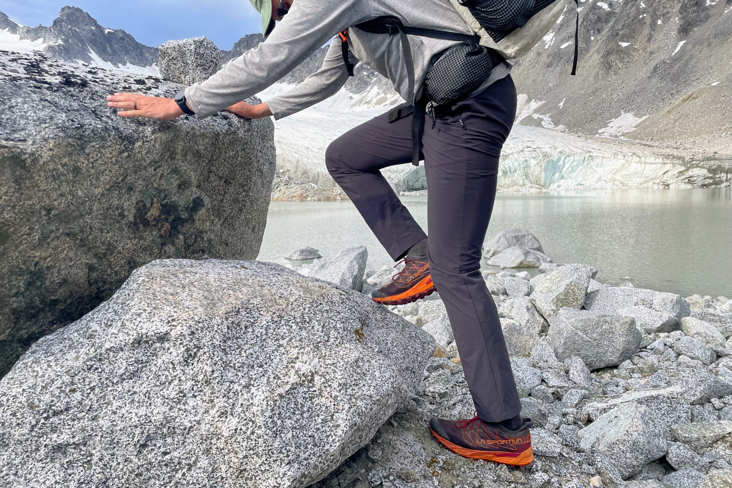 A man climbs up boulders in front of a glacier.