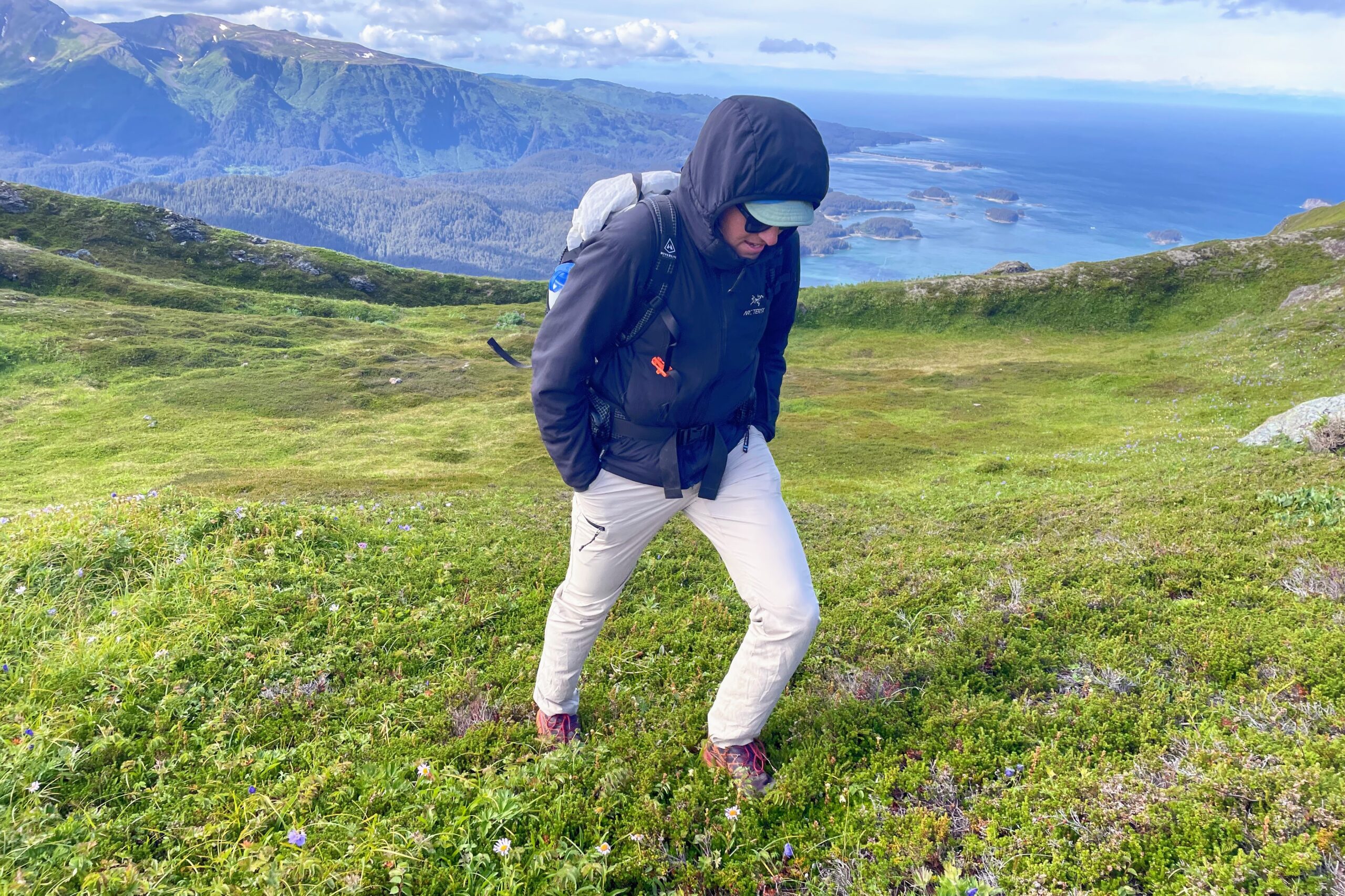 Um homem caminha morro acima com vista para o mar ao fundo