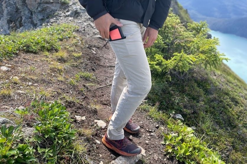 A man puts a cell phone in his pocket on a hiking trail.