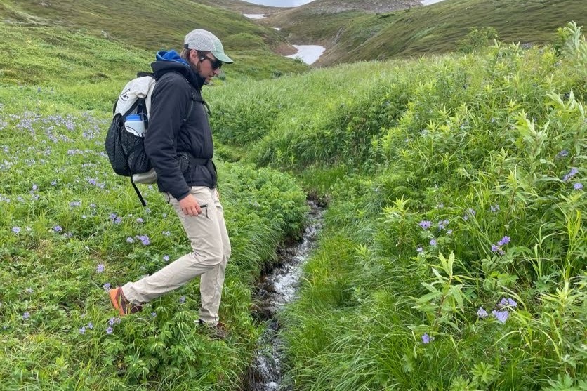 Um homem caminha até um riacho nos Alpes.