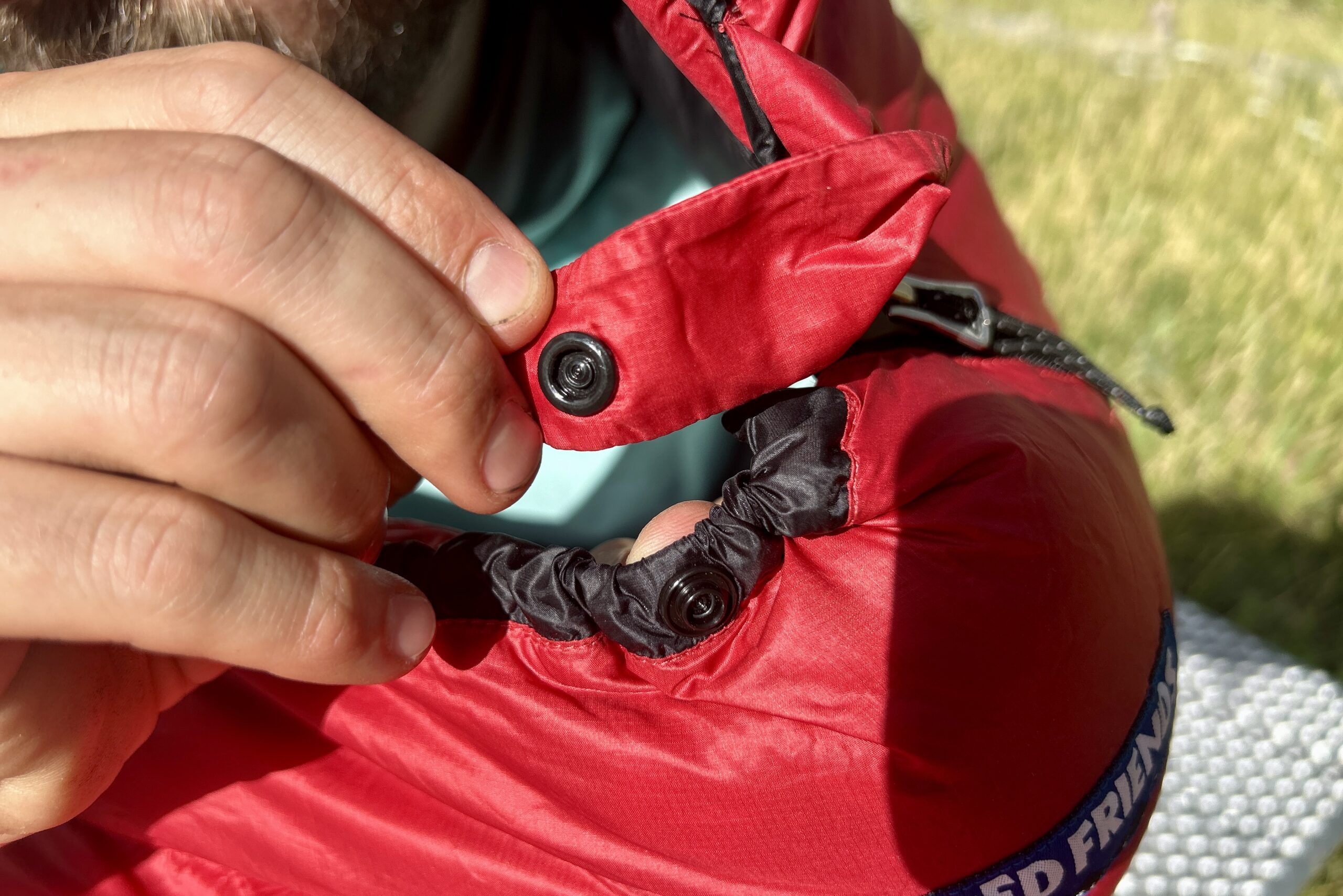 A close-up of the button closure on a sleeping bag at the top of a zipper near the hood.