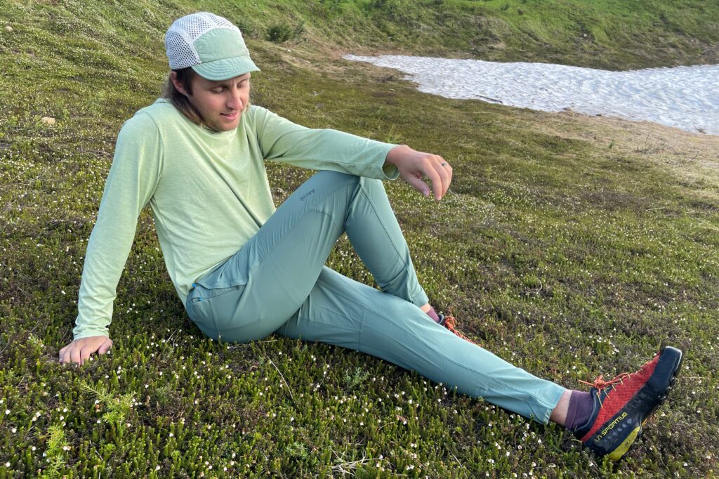 A man stretches while sitting in the tundra with snow in the background.