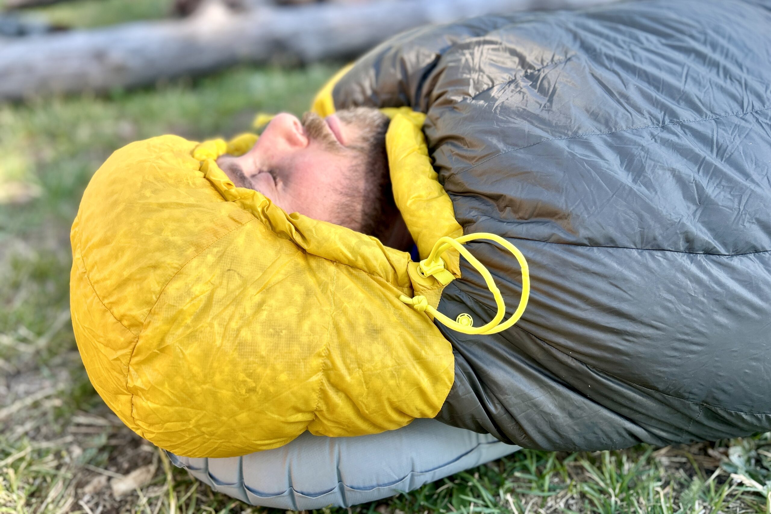 A close-up profile image of a man sleeping a sleeping bag. The hood is cinched tightly around his face.