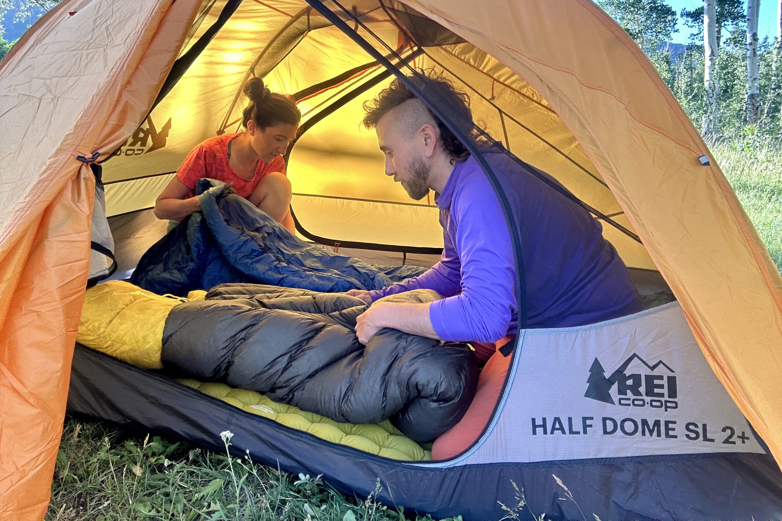 Two people fluff their bags in a yellow tent.