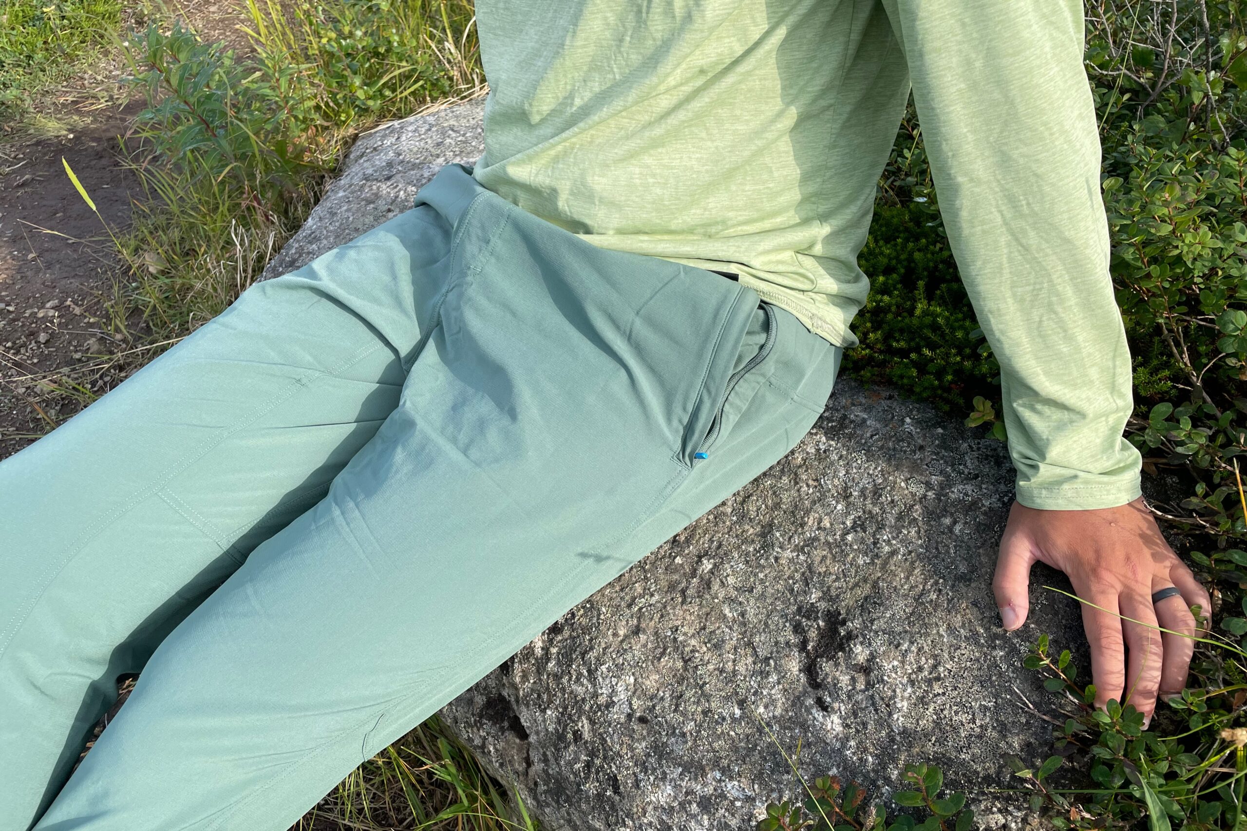 A closeup of sitting on a rock in green pants.