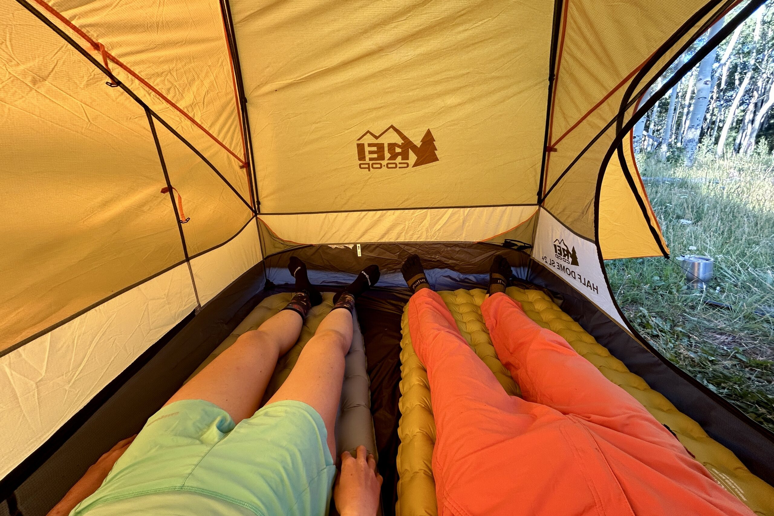 Two people from the waist down lay on sleeping pads in a yellow tent.