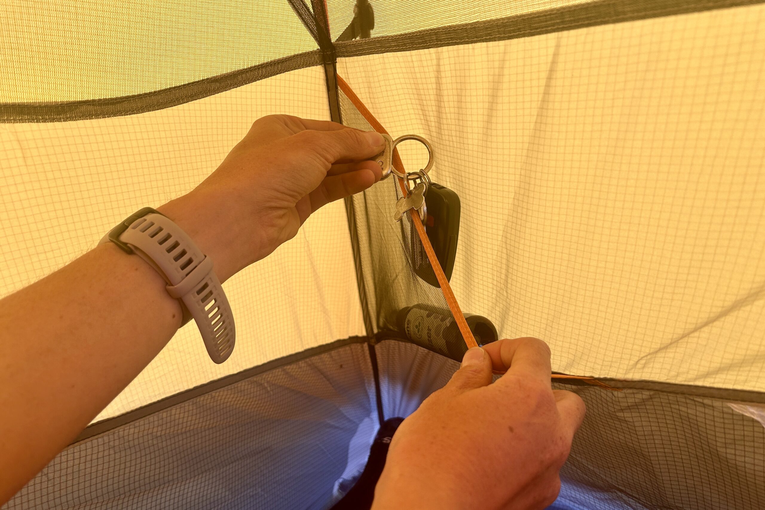 A woman in a yellow tent reaches for a small item in a corner pocket.