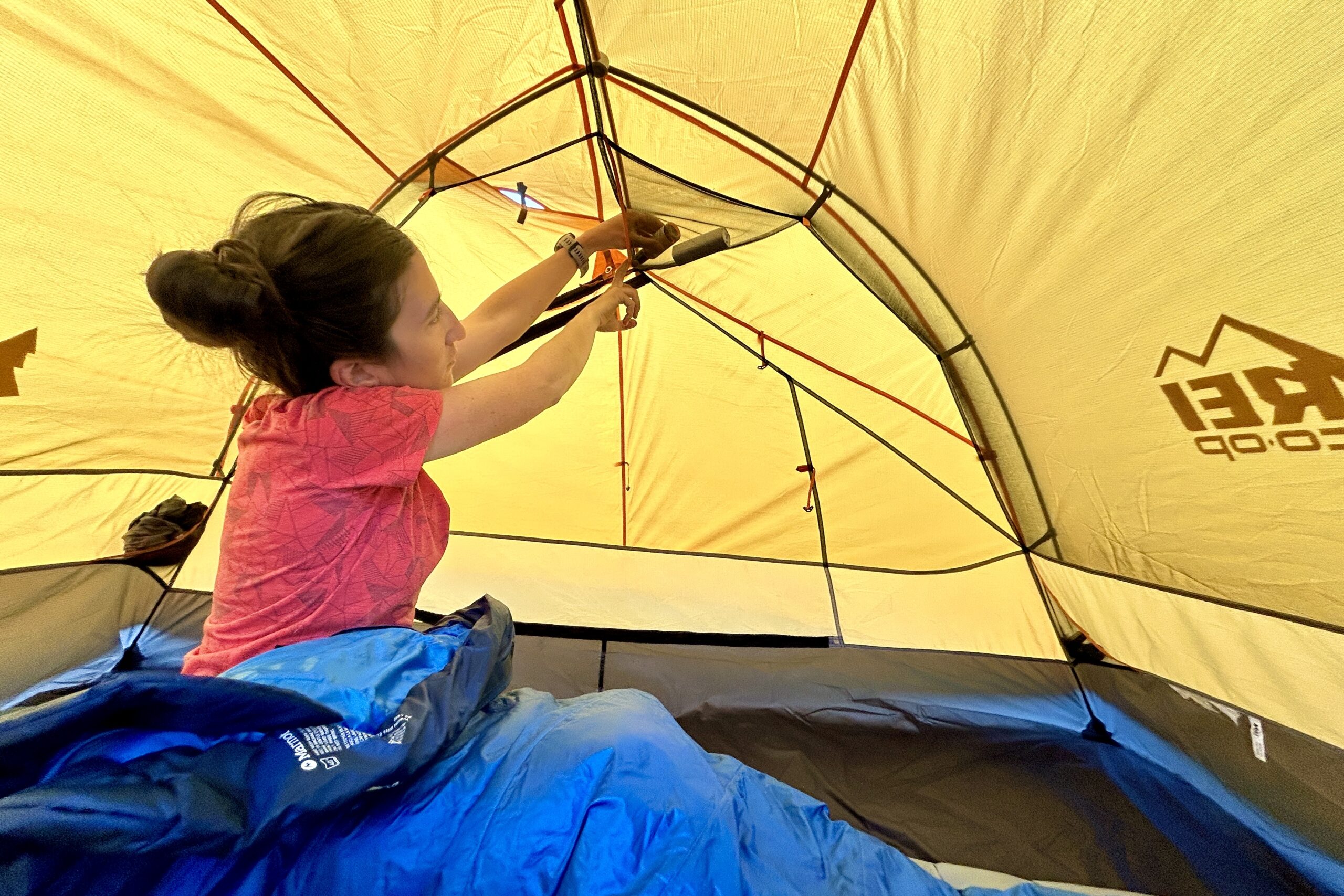 A woman in a yellow tent reaches for something in a ceiling pocket.