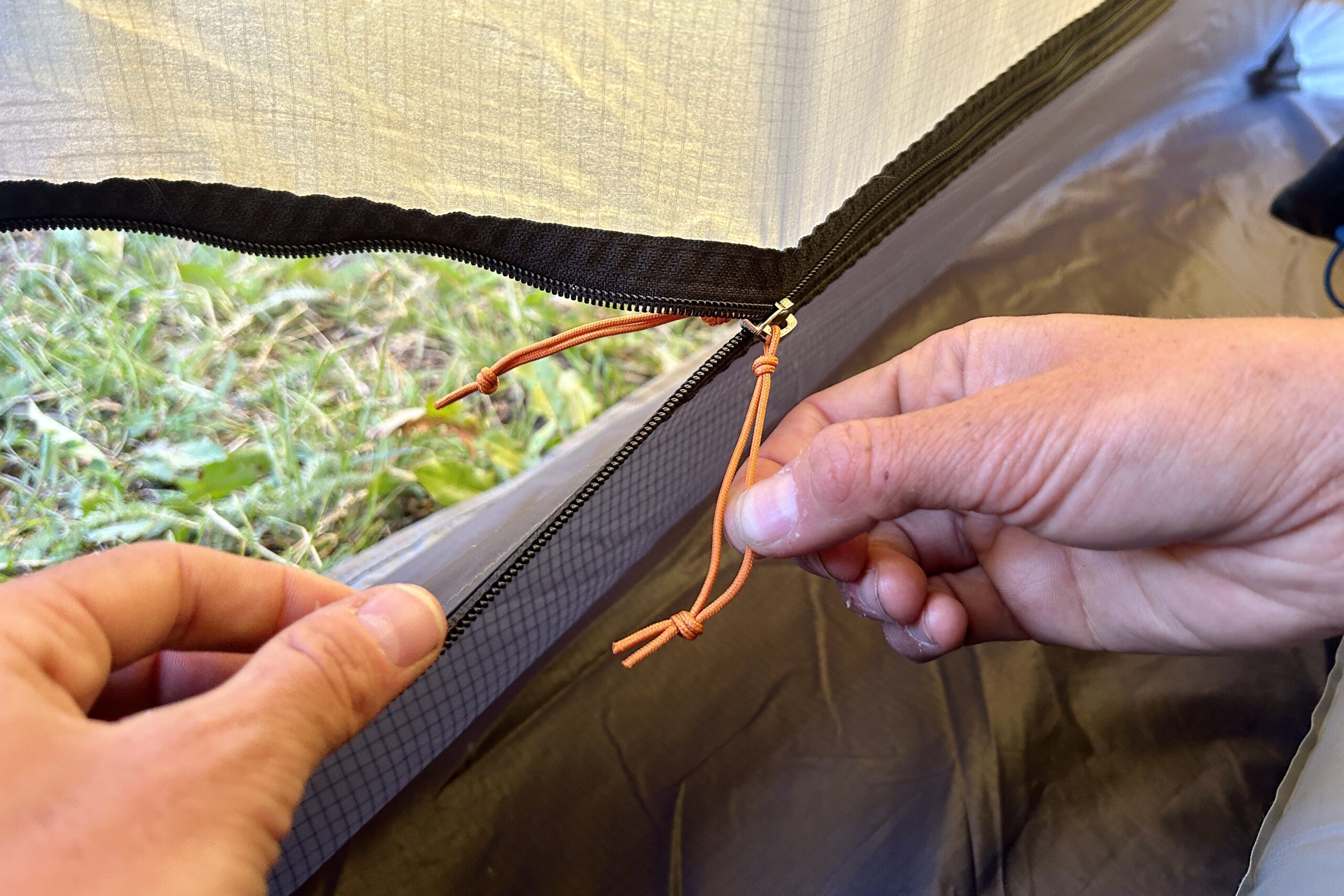 A person zips up a door of a tent with long zipper pulls.