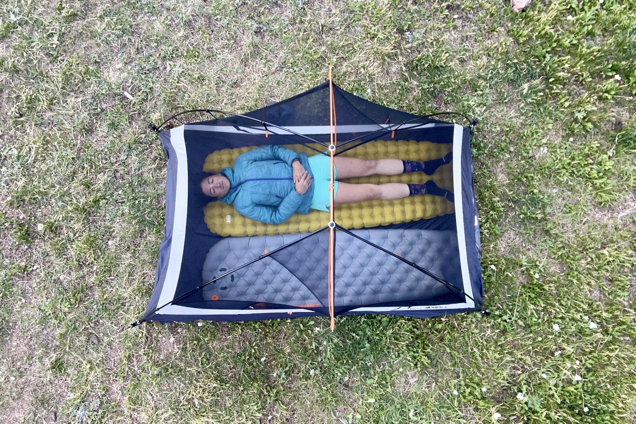 An image from above of a woman laying in a tent with two sleeping pads in a grassy field.