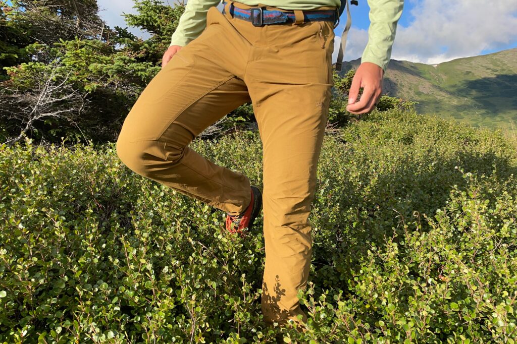 Um homem caminha por entre rochas alpinas com água até as canelas.