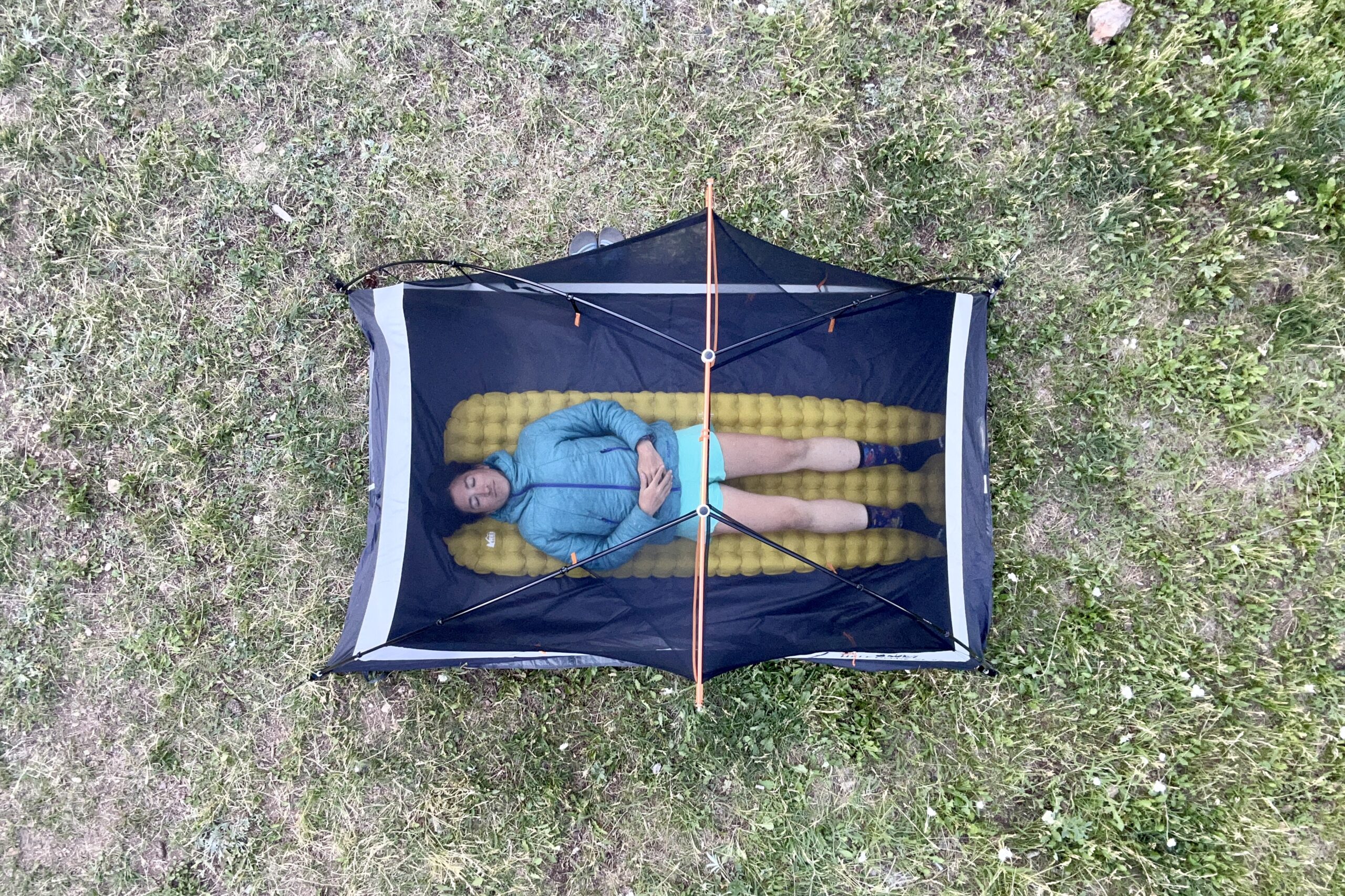 An image from above of a woman laying in a tent on a single sleeping pad in a grassy field.