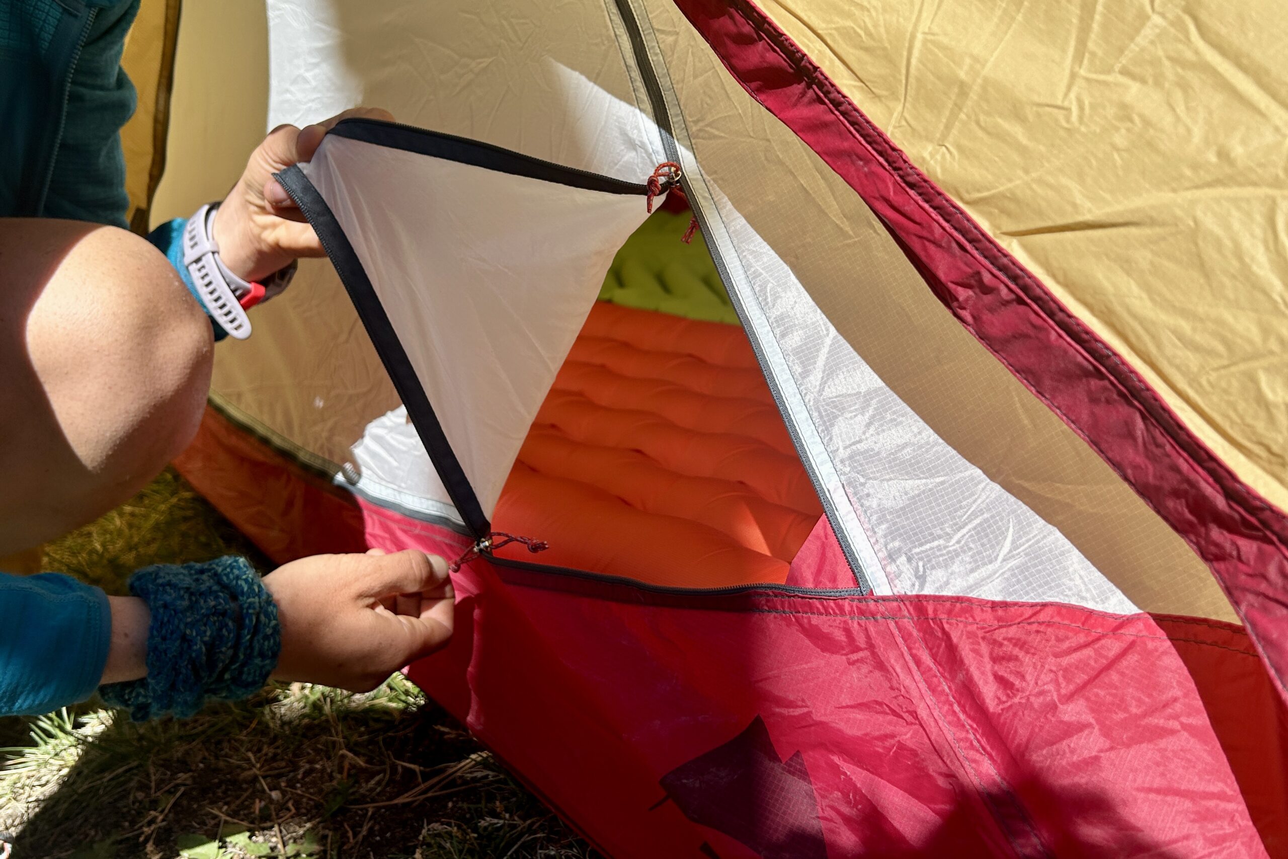 A person opens a tent door using the zipper.