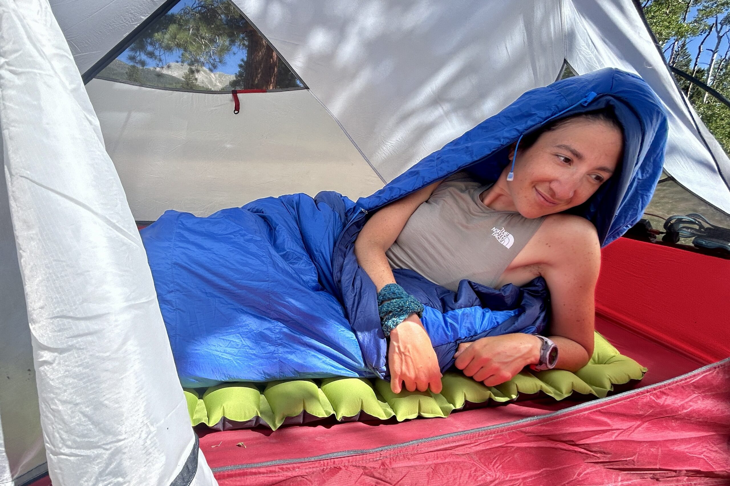 A close-up image of a woman waking up in a tent in the Marmot Trestles 20 sleeping bag in a red tent in the sun.