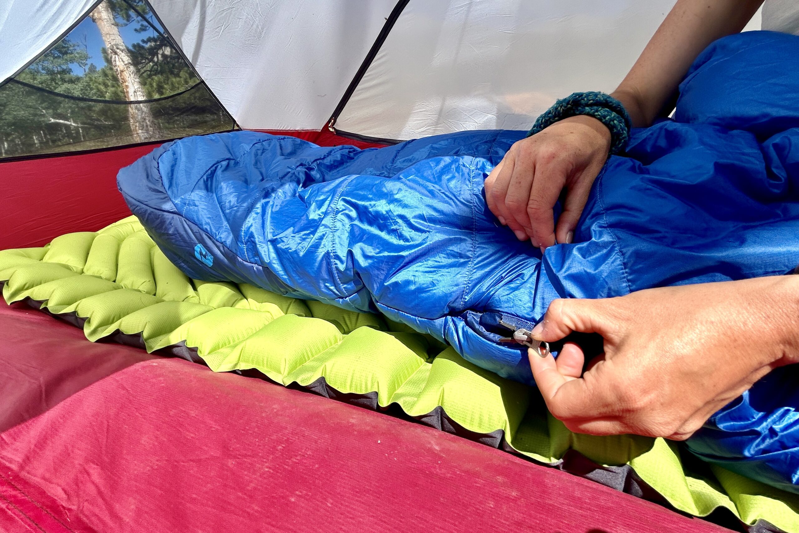 A close-up image of a person zipping up a sleeping bag from the side.