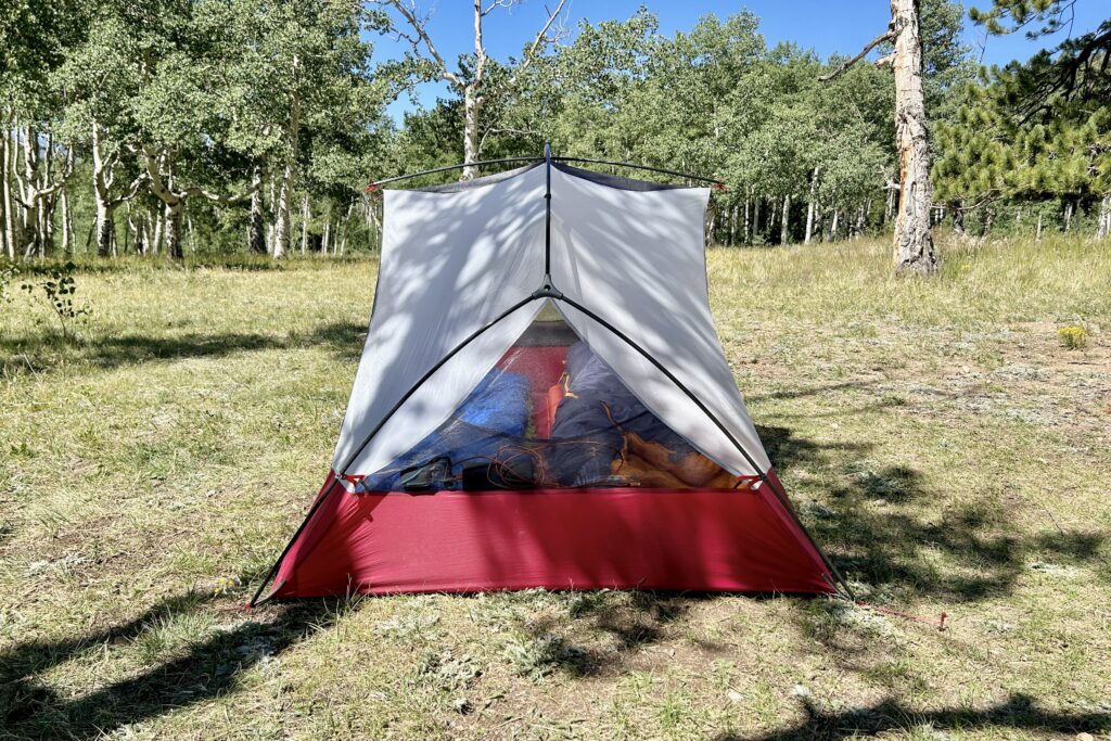 A tent stands alone in the center of a grassy field under a clear blue sky.