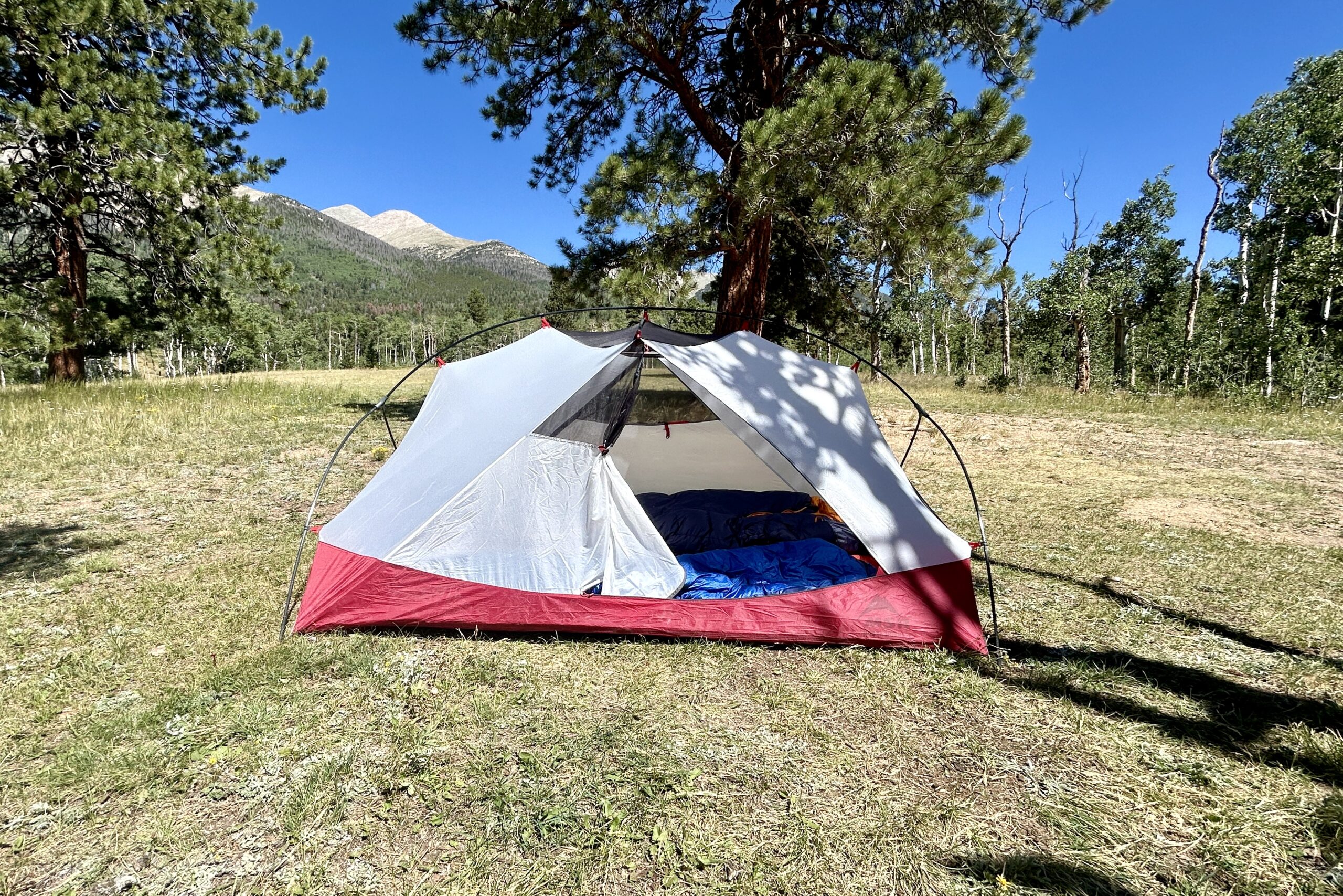 A tent stands alone in the center of a grassy field under a clear blue sky.