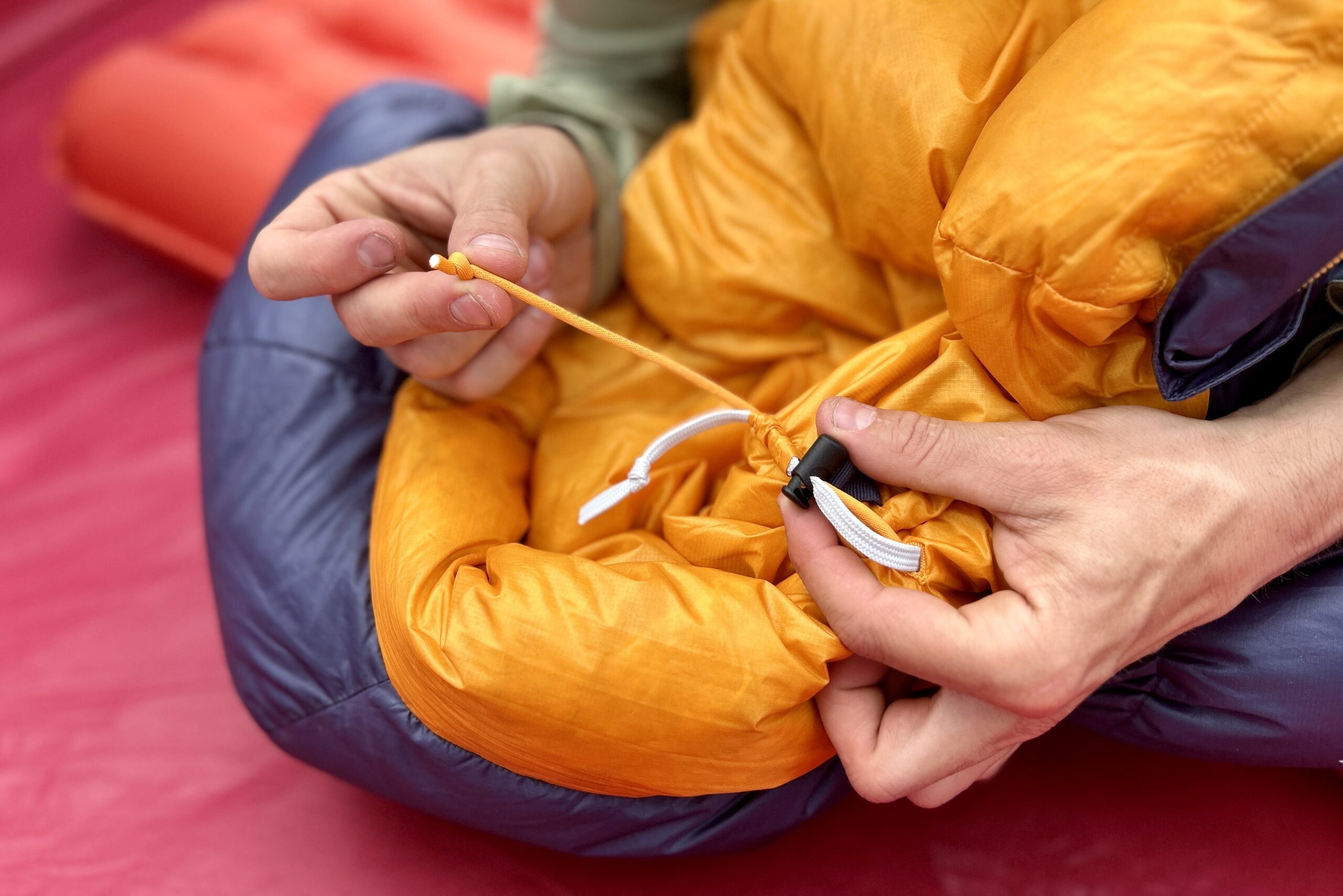 A man tightens up the cinch cord of a sleeping bag with one hand on the string, and the other holding the cinching mechanism.