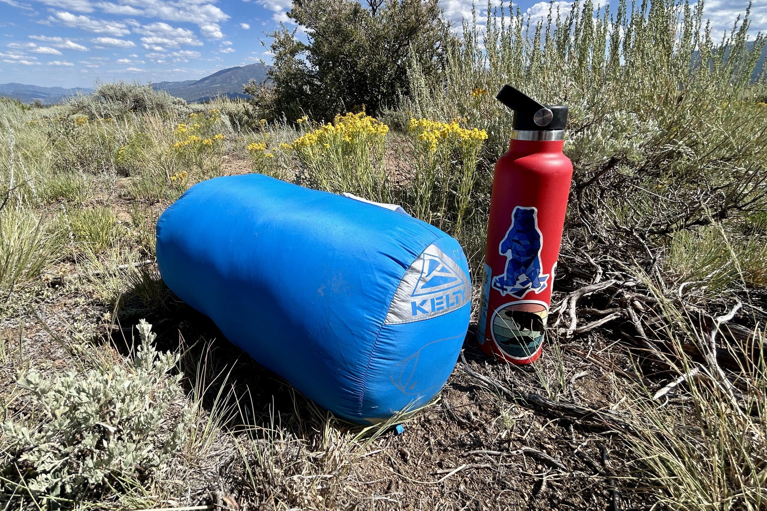 A picture of a sleeping bag in a stuff sack sitting next to a tall, narrow water bottle.