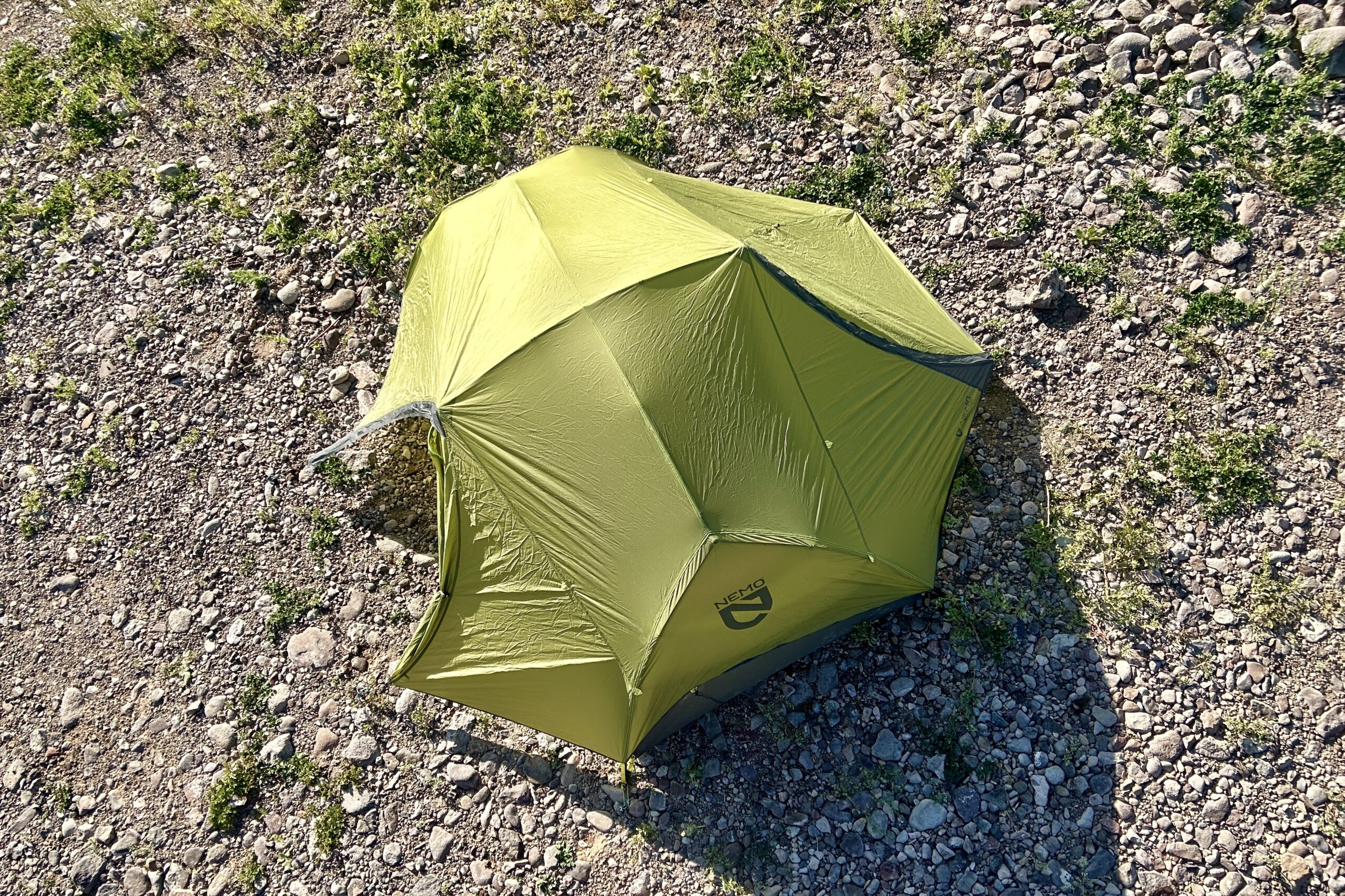 A green tent set up on rocky terrain from above.