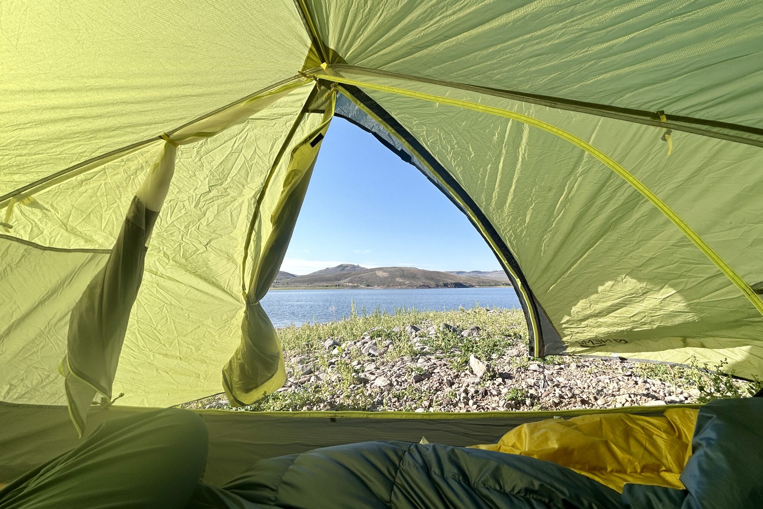 View of a lake through an open rainfly from inside a green tent.