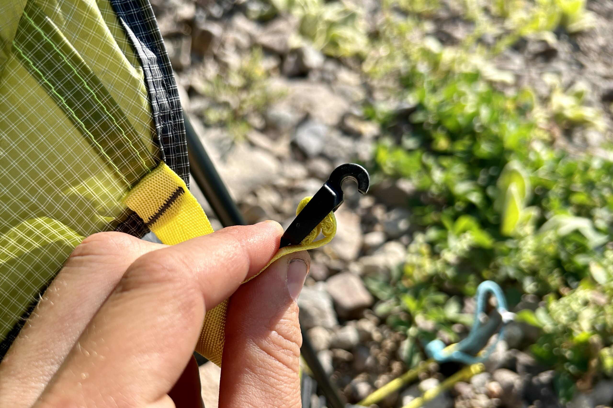 A person uses the hook attachment for the rainfly of a tent.