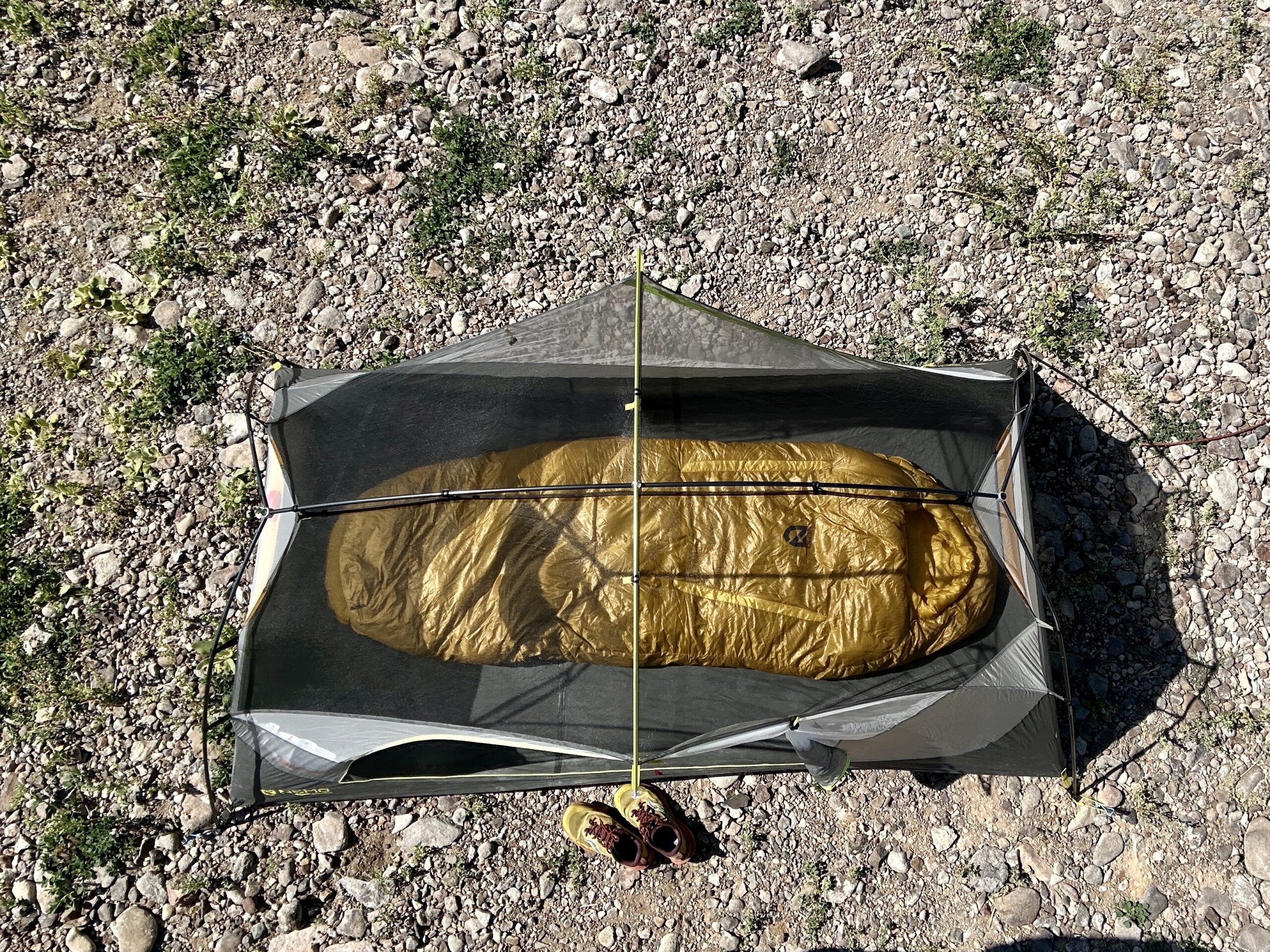 An image of a sleeping bag on a sleeping pad in a tent with a pair of shoes outside. This picture is from about 5 feet above the tent, looking down.