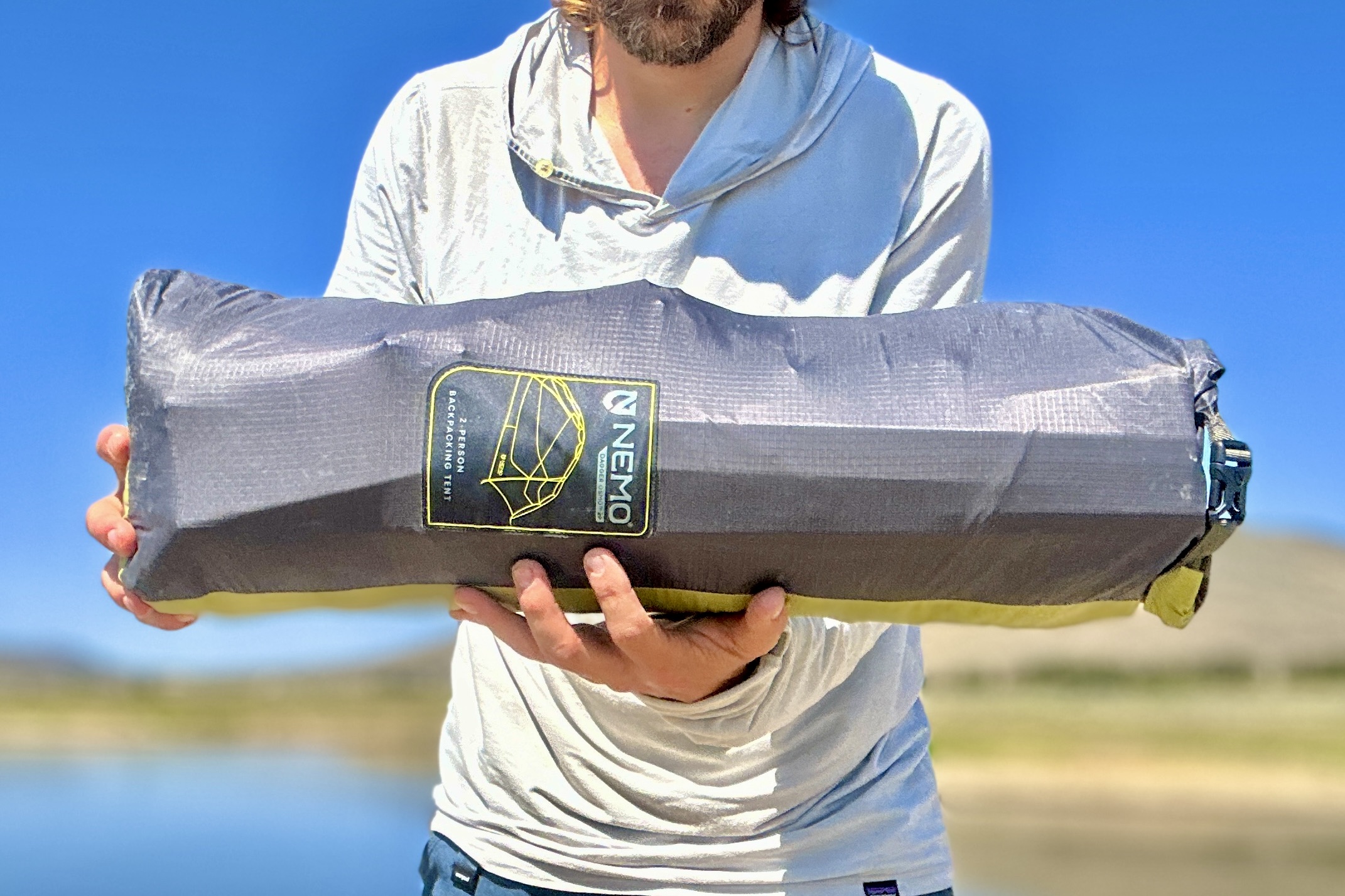 A man holds the packaged NEMO Dagger OSMO 2 with a blue sky in background.