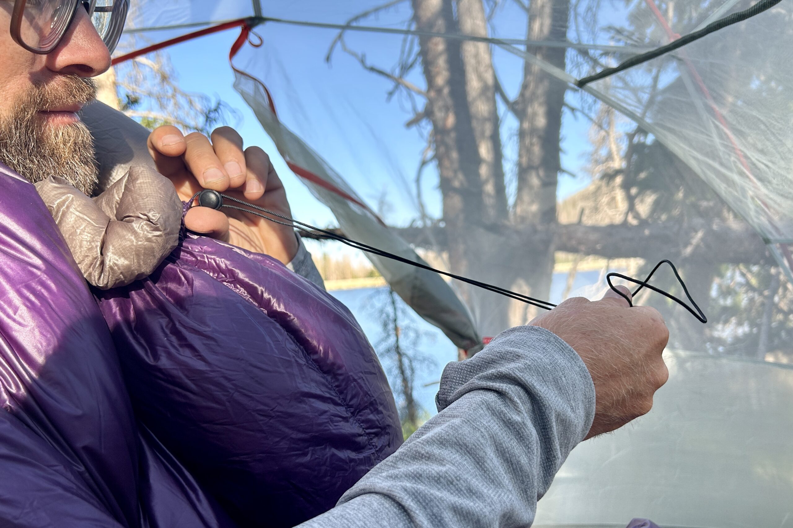 A man tightens a cinch cord around the neck of his sleeping quilt.