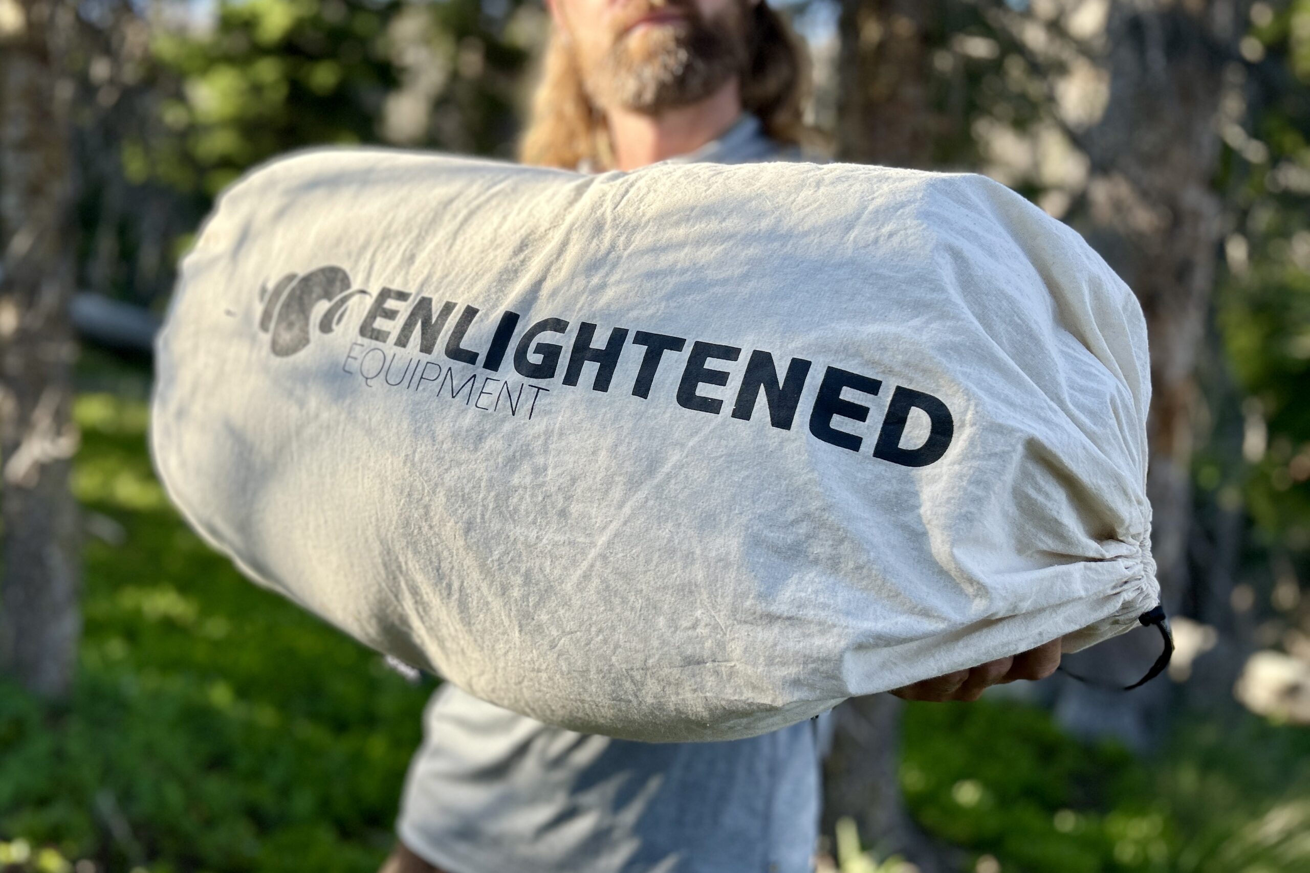 A man holds out the storage sack for an Enlightened Equipment sleeping quilt.