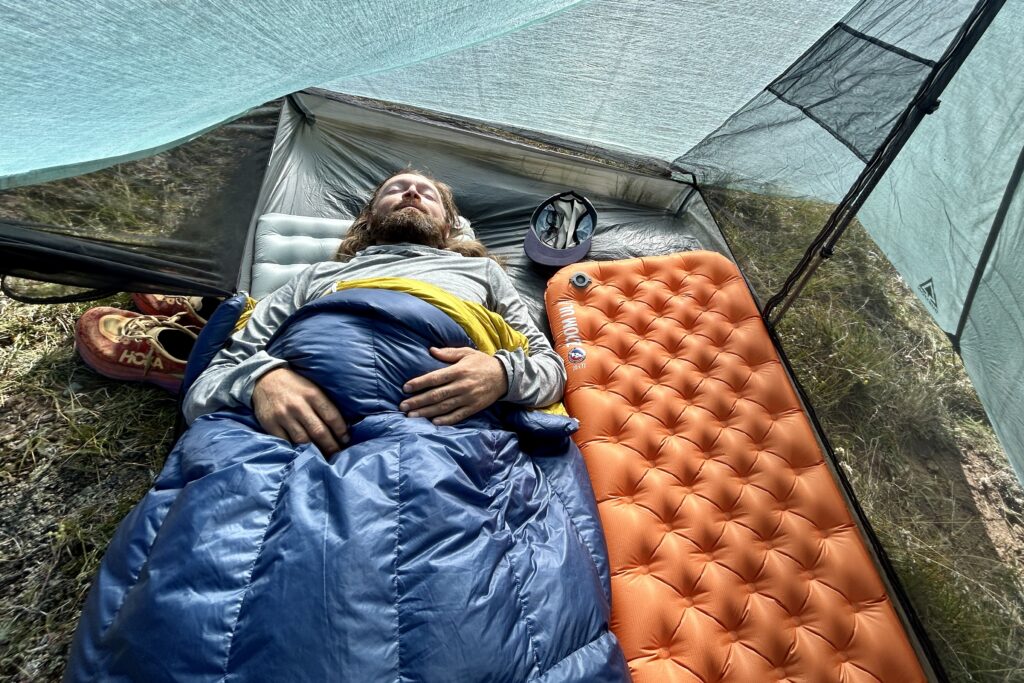 A top-down image of a man sleeping in a tent on a sunny morning.