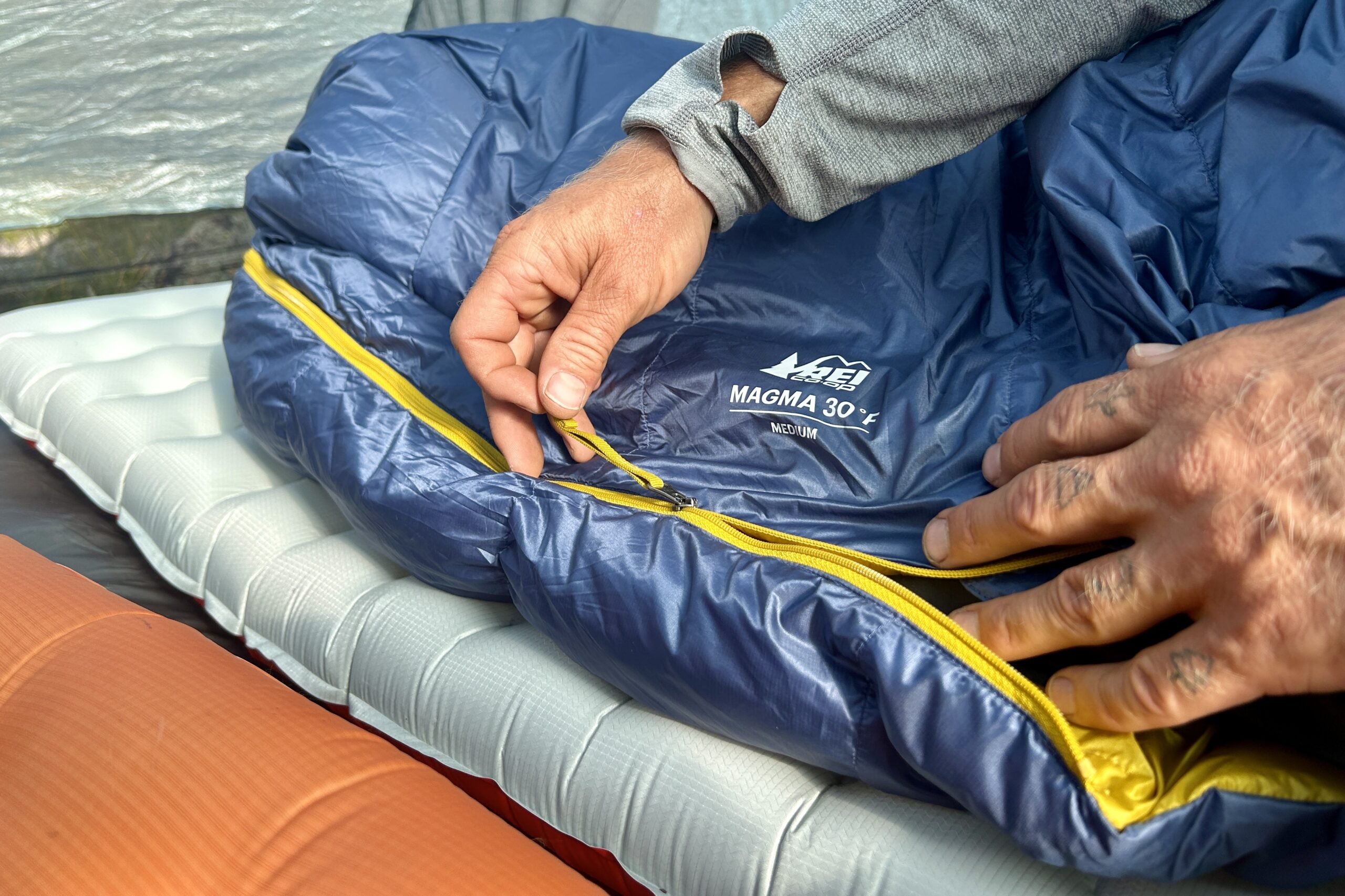 A man zips up a quilt and shoes off the long zipper tab.