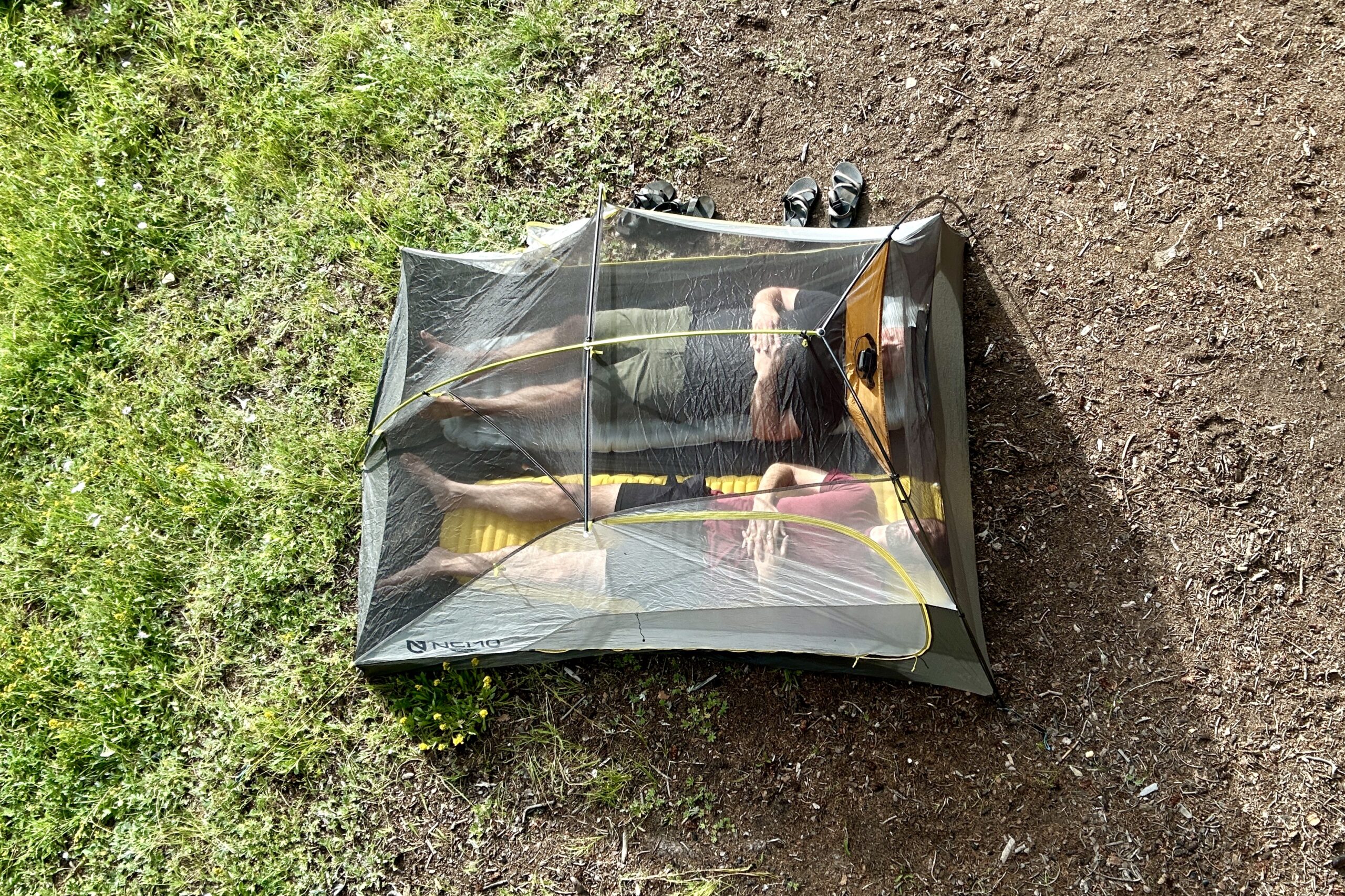 A shot from above of a tent with two men inside, laying on sleeping pads next to each other.