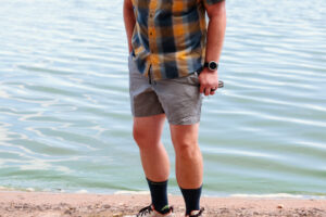 Man standing by a blue lake in hiking shorts.