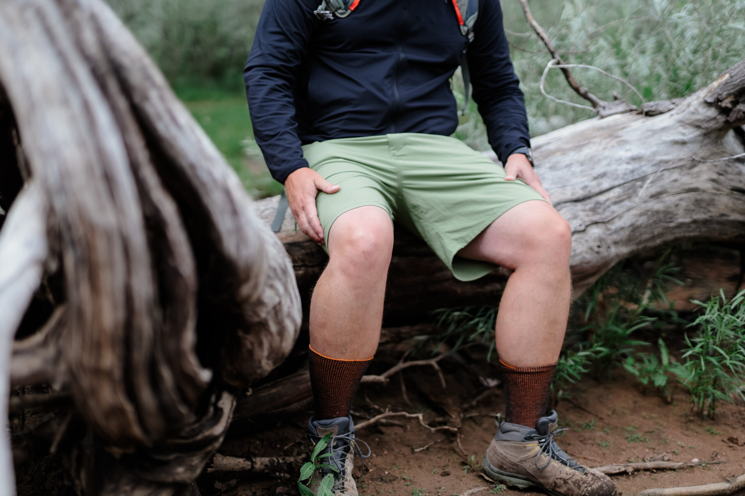 A man sitting on a log in a pair of shorts.