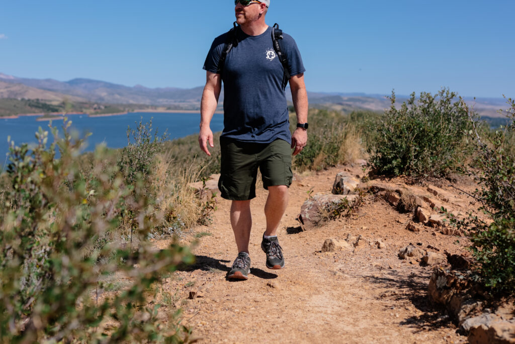 Man walking on trail by lake in shorts.