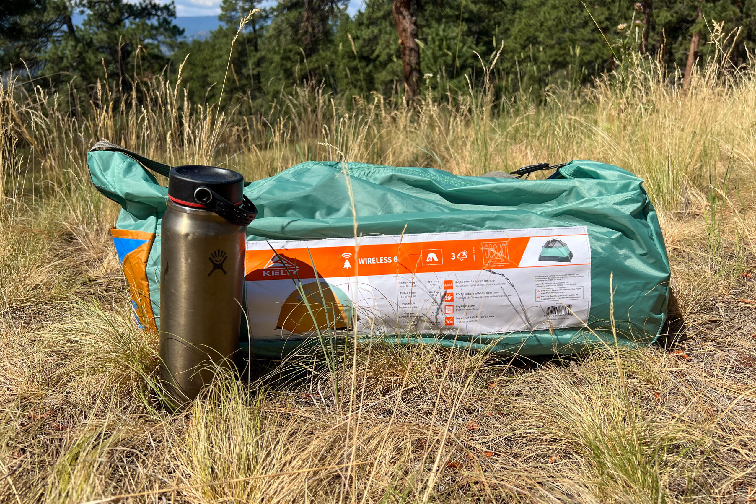 The image shows the original stuff sack next to a standard sized 20 ounce water bottle in a grassy setting.