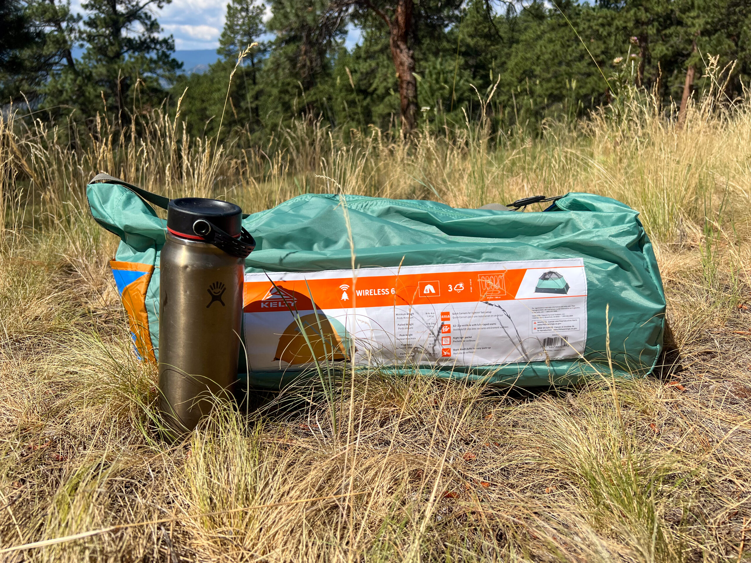 The image shows the original stuff sack next to a standard sized 20 ounce water bottle in a grassy setting.