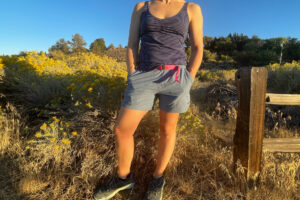 a hiker posing next to a fence in a field of rabbit brush and sage in the sunny high desert