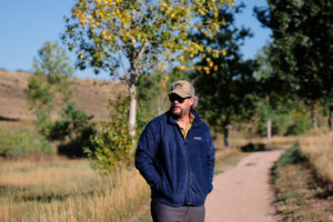 A man in a hat and blue fleece looks off while hiking on a trail.